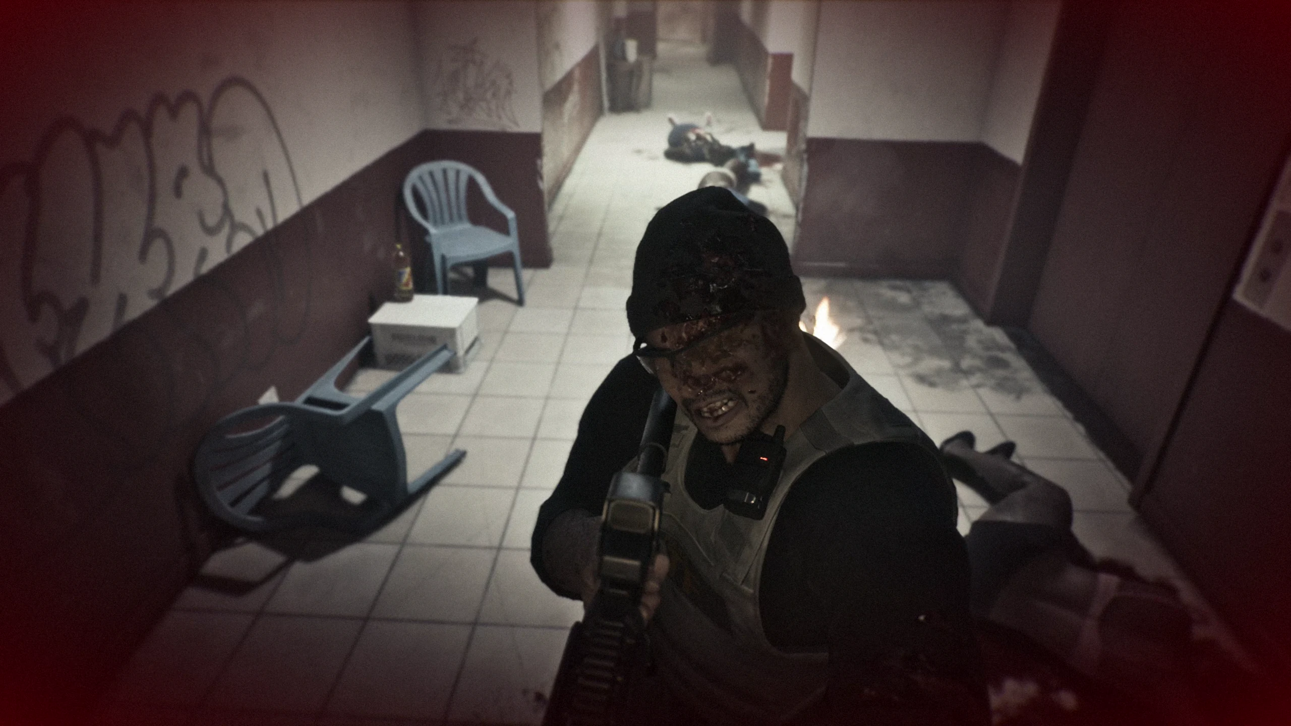 A bloodied enemy in body armour raising a rifle at close range in a tiled corridor, with bodies and fire further down the hall