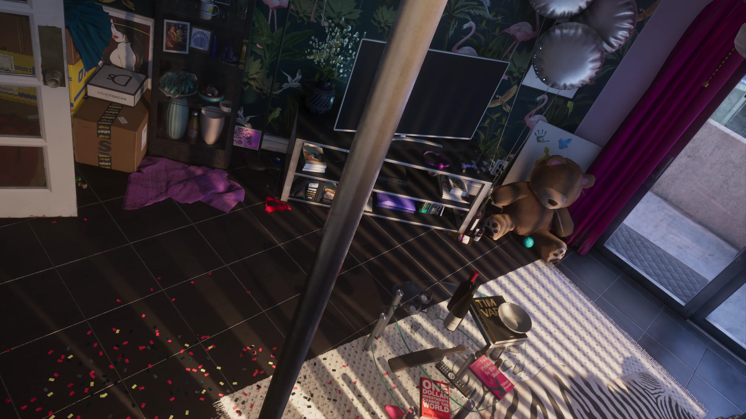 Overhead view of a cluttered safehouse interior, with confetti across the floor, balloons, bottles and a teddy bear